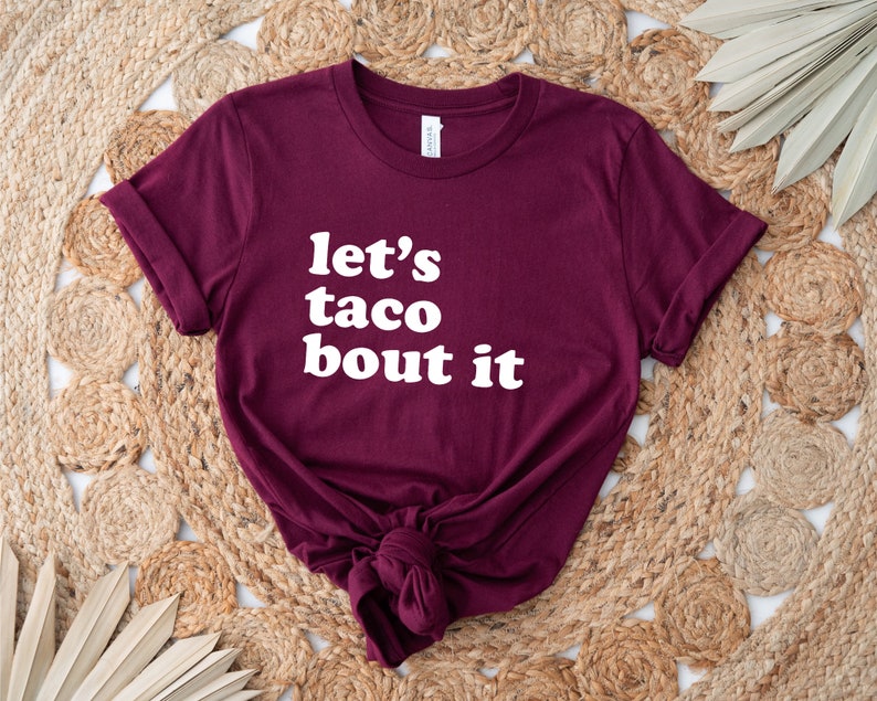 May include: Burgundy t-shirt with white text that reads "let's taco bout it".