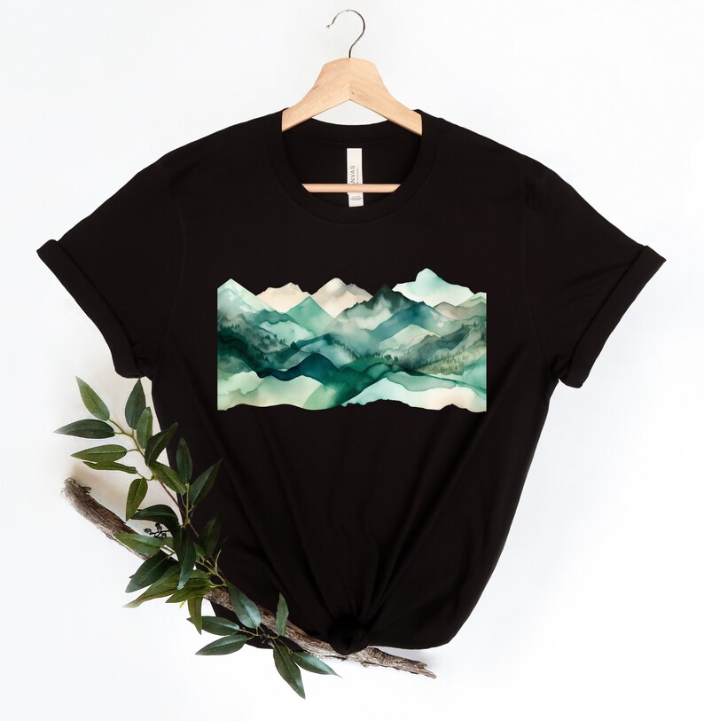 Puede incluir: Camiseta negra con un dise&ntilde;o de acuarela de monta&ntilde;as verdes y azules.