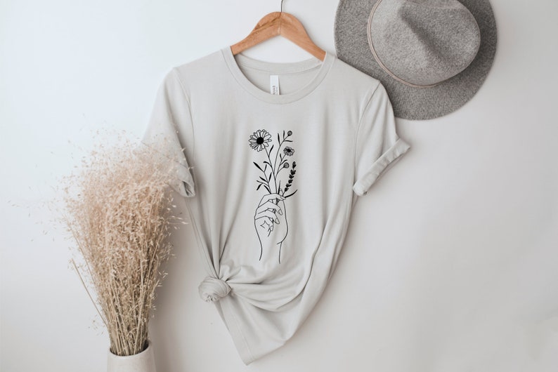 May include: A light gray t-shirt with a black line drawing of a hand holding a bouquet of flowers.
