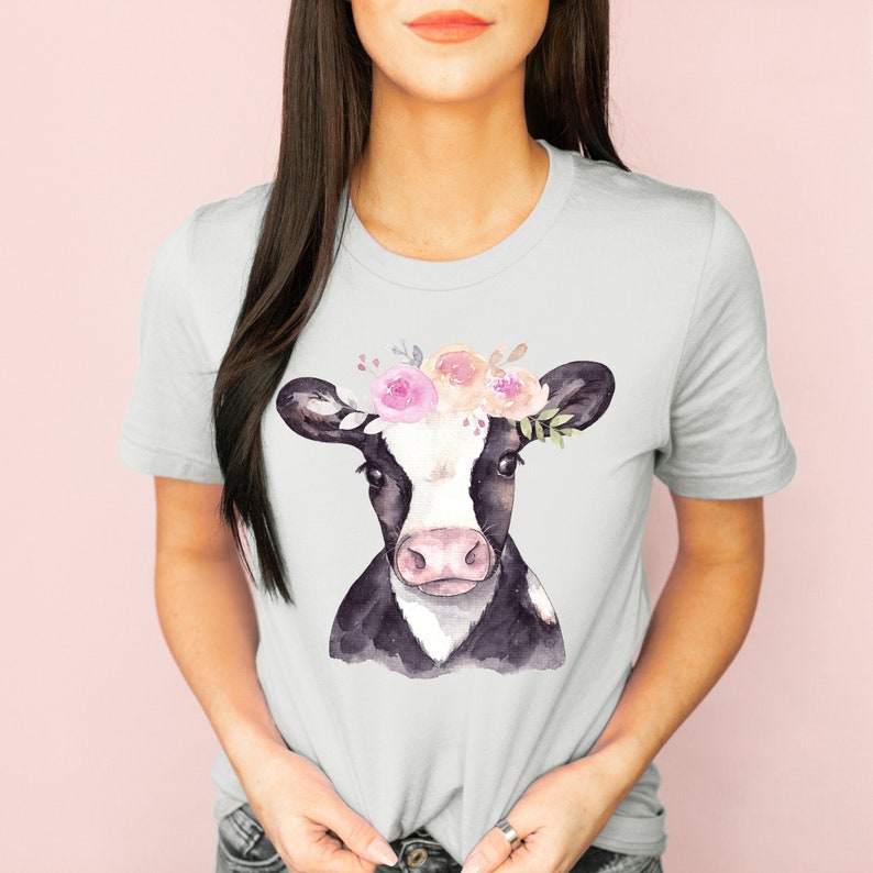 A short sleeve crew neck t shirt with a watercolor cow design. The cow has pink flowers on top of it's head. The shirt is the Bella and Canvas 3001 unisex jersey tee. Very soft and high quality. The color pictured is silver.