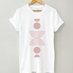 May include: White t-shirt with a pink geometric design featuring stacked circles, half circles, and a curved line pattern.