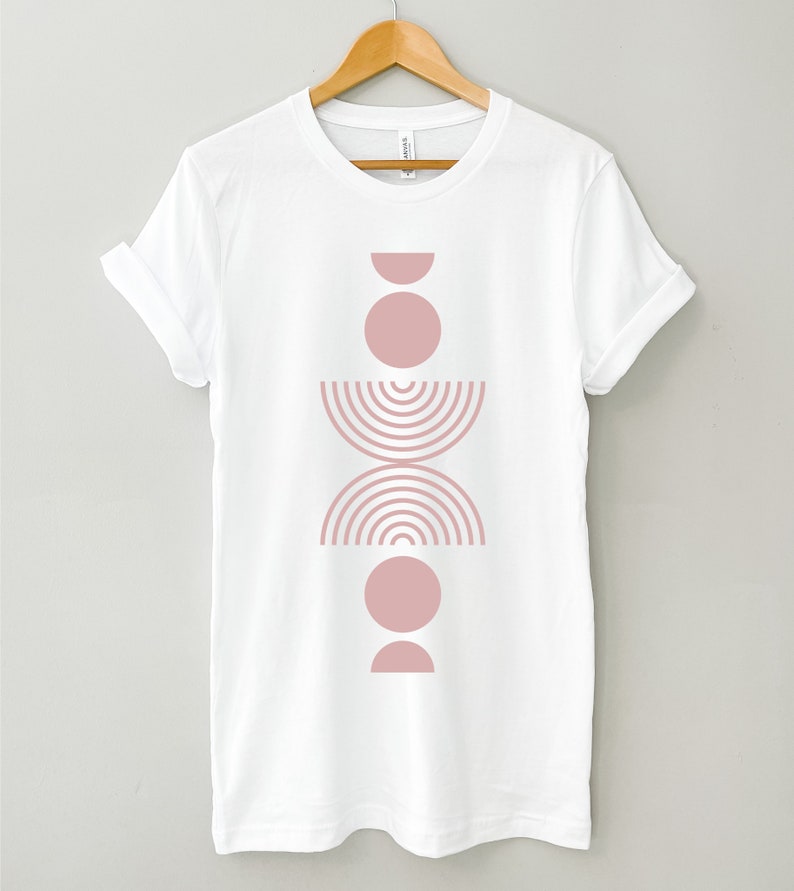 May include: White t-shirt with a pink geometric design featuring stacked circles, half circles, and a curved line pattern.