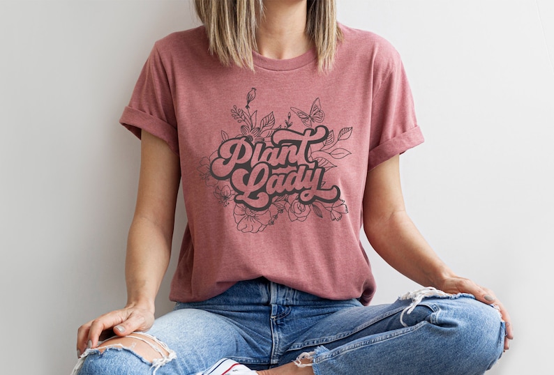May include: A mauve t-shirt with a black graphic design that says "Plant Lady" with a floral design around the text.