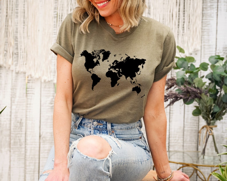 May include: A woman wearing a green t-shirt with a black world map graphic. She is wearing blue jeans with a distressed look.