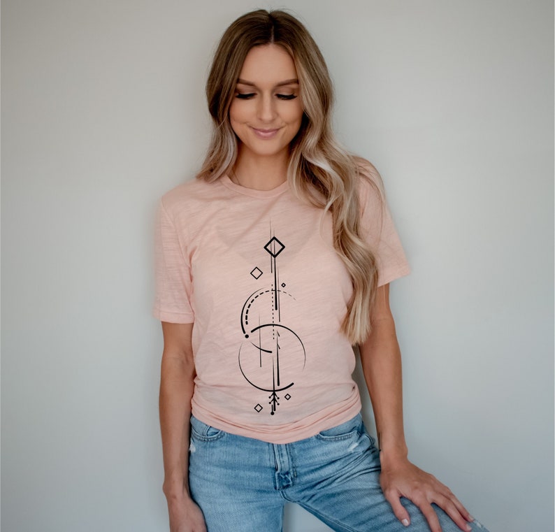 Pode incluir: Uma mulher vestindo uma camiseta rosa claro com um design geom&eacute;trico preto. O design apresenta uma forma de diamante, c&iacute;rculos e linhas.