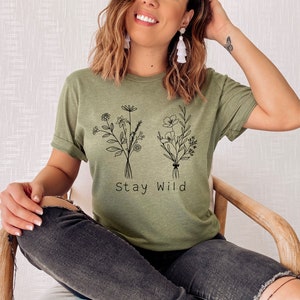 May include: A green t-shirt with a black line drawing of two bouquets of flowers and the text "Stay Wild".