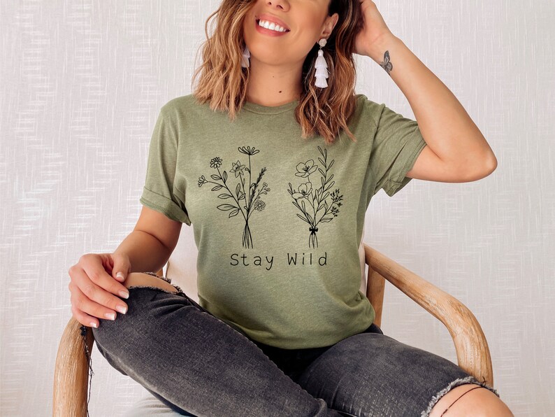 May include: A green t-shirt with a black line drawing of two bouquets of flowers and the text "Stay Wild".