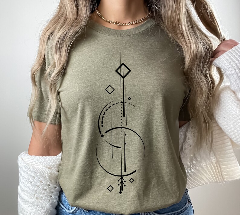 Pode incluir: Uma camiseta verde com um design geom&eacute;trico em preto. O design apresenta uma linha vertical com uma forma de diamante na parte superior, um c&iacute;rculo com uma linha tracejada e uma forma de diamante menor na parte inferior.