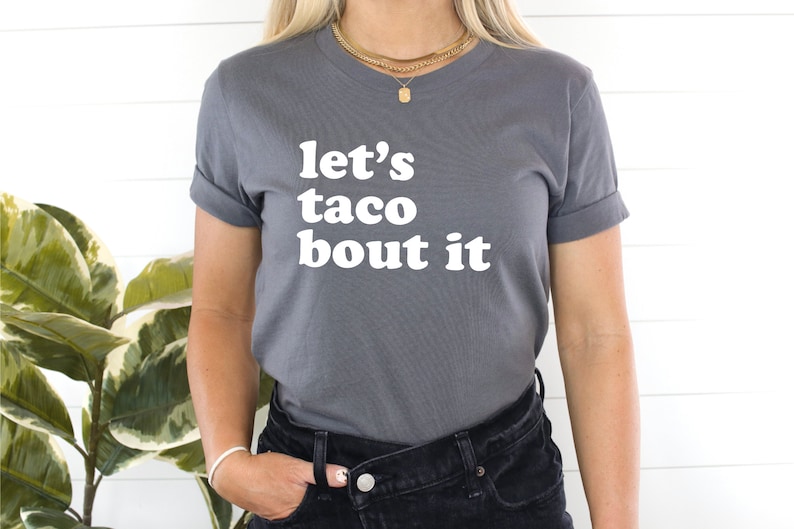 May include: A grey t-shirt with the text "let's taco bout it" in white.