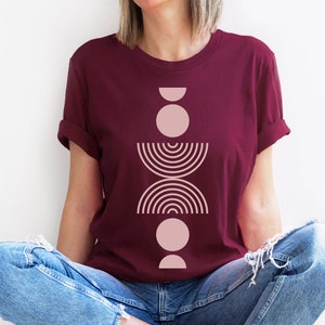 May include: A maroon t-shirt with a pink geometric design featuring circles, half circles, and arcs.