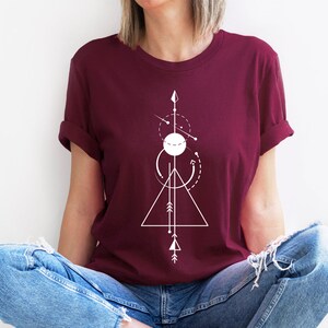 May include: A maroon t-shirt with a white geometric design featuring a triangle, circle, and arrows.