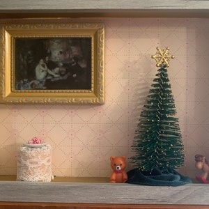 May include: A framed shadow box with a small painting, a miniature Christmas tree with a gold snowflake topper, a teddy bear, a small cake with red candies, and a rocking horse.