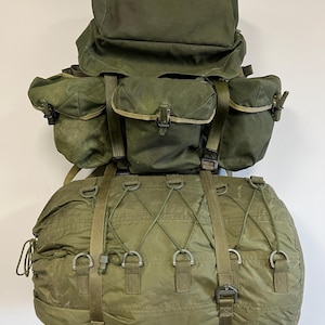 May include: A green canvas military backpack with two large side pockets and a smaller top pocket. A green canvas duffel bag is attached to the bottom of the backpack.
