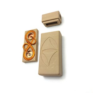 May include: A tan-colored, rectangular ceramic box with a lid and a separate piece. One piece has an embossed design, and another has copper wire detailing. The pieces are arranged on a white surface.