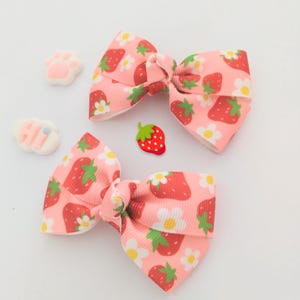 May include: Two pink hair bows with a strawberry and white flower pattern.