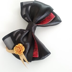 May include: A black satin bow with a red and black patterned ribbon and a gold rose accent.