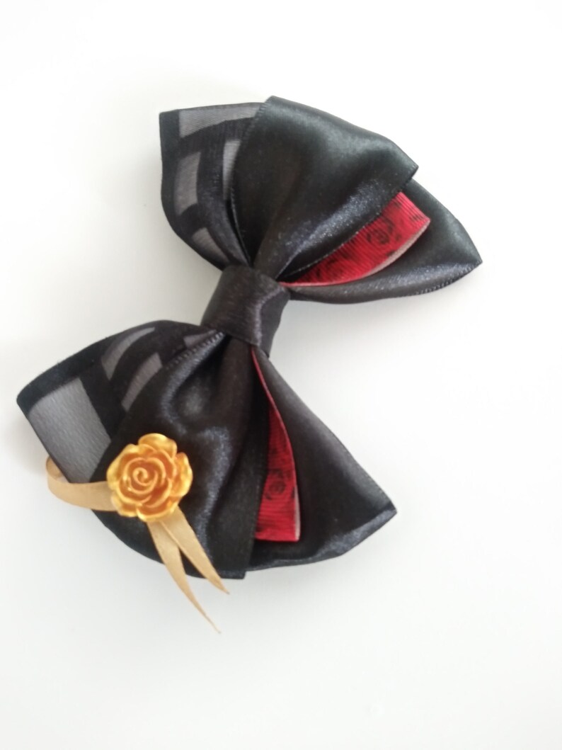 May include: A black satin bow with a red and black patterned ribbon and a gold rose accent.