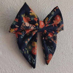 May include: A large, navy blue bow with a floral pattern in orange, yellow, and white. The bow is tied in the center and has two large loops and two pointed ends. The fabric has a Japanese-inspired design.