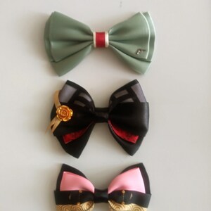 May include: Three different bow ties. The top bow tie is green with a red stripe. The middle bow tie is black with a red and gray pattern and a gold flower accent. The bottom bow tie is black with a pink and gold pattern.
