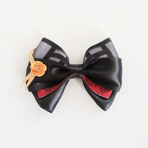 May include: A black satin bow with a red and black patterned ribbon and a gold rose accent.