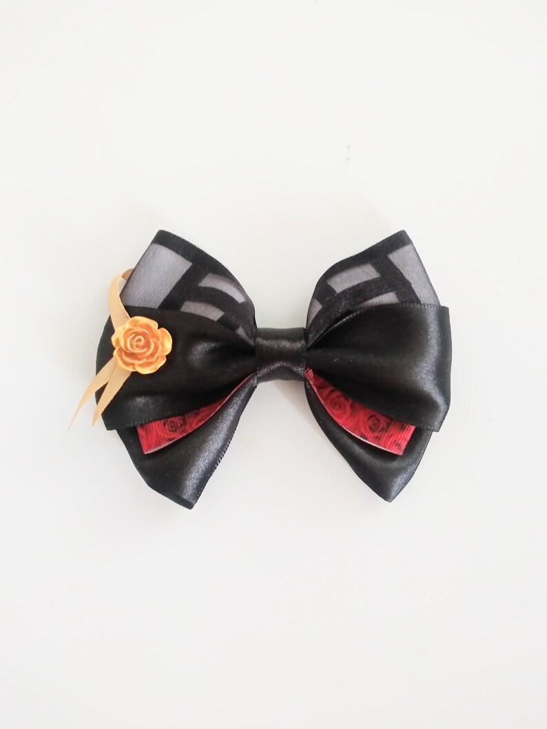 May include: A black satin bow with a red and black patterned ribbon and a gold rose accent.