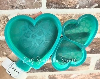 May include: A teal-colored silicone mold shaped like two interlocking hearts. The mold has a pattern of small hearts embossed on the inside.