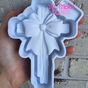 May include: A light blue cross-shaped mold with a bow design. The mold is made of plastic and has a detailed texture. The text "Ems Southern Scents" is visible in the upper right corner.