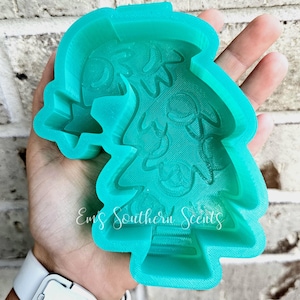 Puede incluir: Un molde de silicona verde azulado con forma de árbol de Navidad con una estrella en la parte superior. El molde tiene una superficie texturizada con un diseño de adornos y ramas de pino. El texto "Emi's Southern Scents" es visible en el molde.