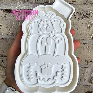 Op de afbeelding: Een witte, pompoenvormige koekjessnijder van plastic met een pompoengezicht en een rechthoekige bovenkant. De koekjessnijder heeft een gelaagd ontwerp en wordt in een hand gehouden. De tekst "Southern Scents" is zichtbaar.