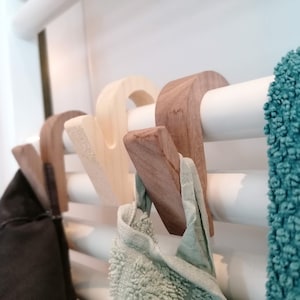 Könnte beinhalten: Haken aus Holz, die an einem weißen Handtuchhalter befestigt sind. Ein türkisfarbenes Handtuch hängt am rechten Haken und ein hellgrünes Handtuch hängt am linken Haken.