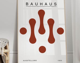 May include: A light brown wicker chair with a white throw blanket sits on a natural fiber rug in front of a white wall. A framed poster with the text "BAUHAUS AUSSTELLUNG 1923" and a red abstract design hangs on the wall.