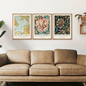 May include: Three framed prints of floral patterns by William Morris. The prints are in a light blue, yellow, and green color scheme, a red, white, and green color scheme, and a blue, gold, and green color scheme. The prints are hanging on a white wall above a brown leather couch.