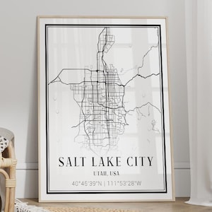 May include: A framed vertical wall art print featuring a black and white street map of Salt Lake City, Utah, USA, with the text "SALT LAKE CITY UTAH, USA" and coordinates "40°45'39"N | 111°53'28"W" printed in a clean, black sans-serif font on a white background.