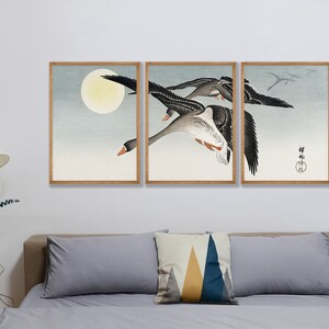 May include: A triptych of framed art prints featuring a flock of geese in flight against a pale blue sky and a full moon. The artwork has a traditional Japanese aesthetic, with muted colors and a minimalist style.