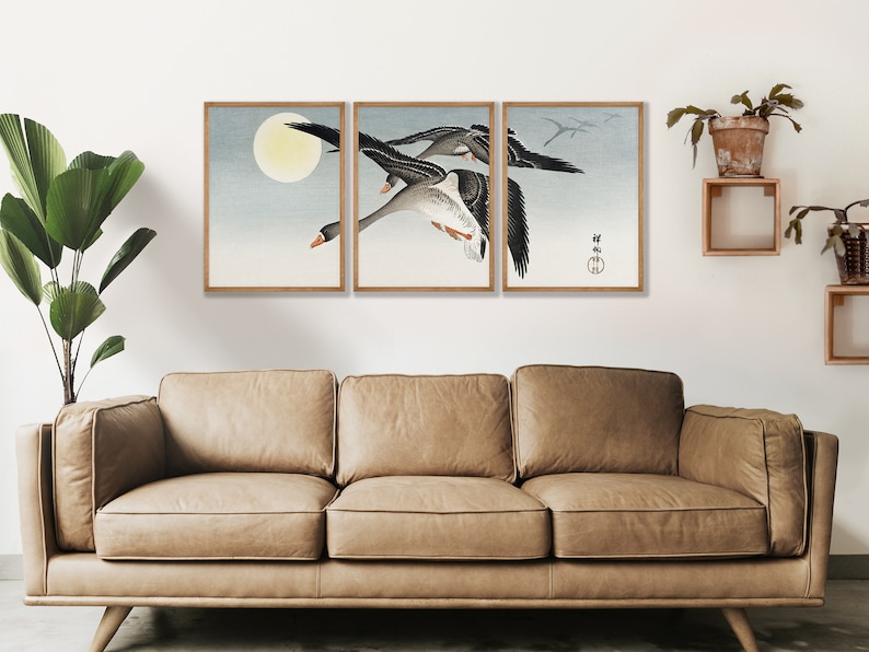 May include: Three geese flying in formation against a light blue sky with a full moon in the background. The geese are black and white with long necks and wings outstretched. The image is framed in a wooden frame.