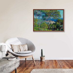 May include: A framed painting of a landscape scene with a view of a town from a hilltop. The painting is done in a style reminiscent of Impressionism, with visible brushstrokes and a focus on light and color. The scene is dominated by a lush green forest in the foreground, with a glimpse of a blue sea and a town in the distance.
