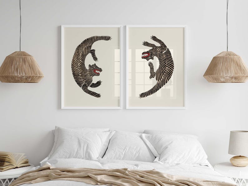 May include: Two black and white stylized illustrations of a tiger in a circular pose, framed in white and hung on a white wall above a bed with white bedding.