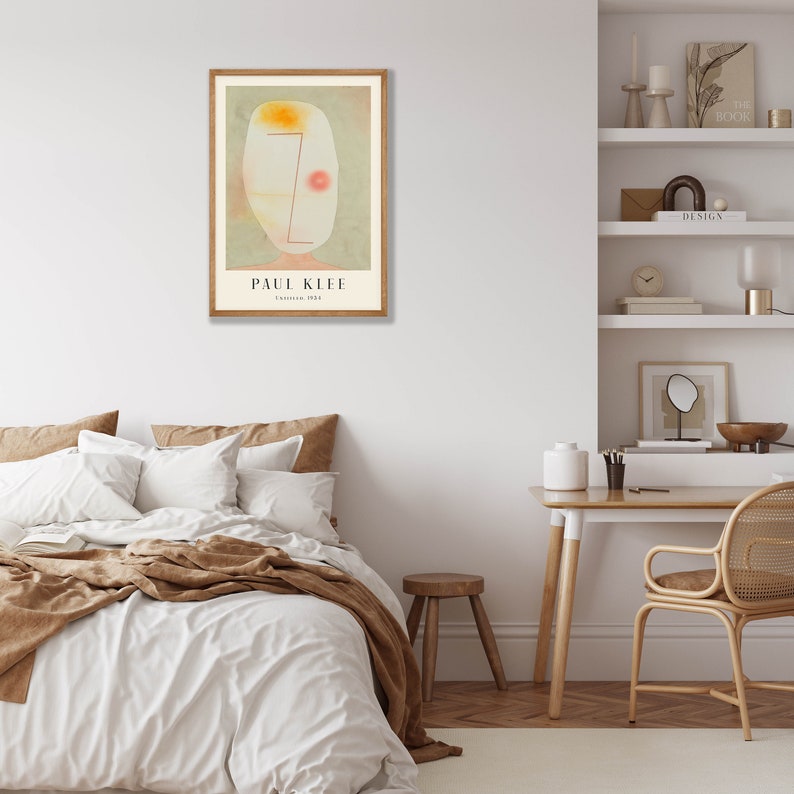 May include: A framed art print featuring a Paul Klee painting titled Untitled, 1924. The artwork displays an abstract, pale, oval-shaped face with a single red dot, a yellow patch, and thin red lines on a muted green background, all set in a wooden frame.