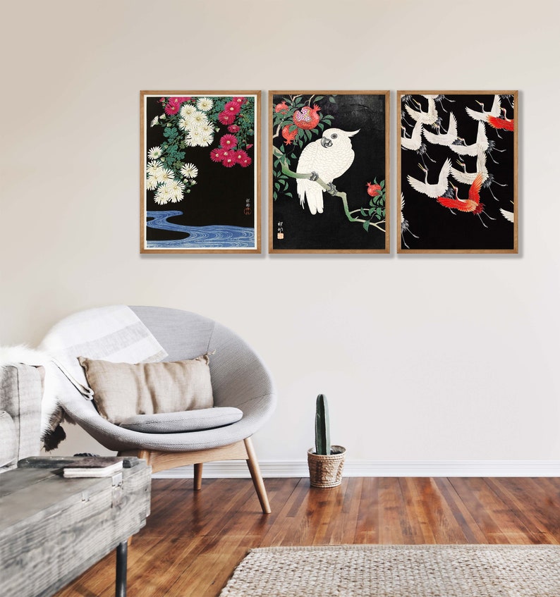 K&ouml;nnte beinhalten: Drei gerahmte Drucke mit japanisch inspirierten Kunstwerken. Der erste Druck zeigt wei&szlig;e Blumen auf schwarzem Hintergrund mit einem blauen Fluss. Der zweite Druck zeigt einen wei&szlig;en Kakadu, der auf einem Ast mit roten Granat&auml;pfeln sitzt. Der dritte Druck zeigt rote und wei&szlig;e Kraniche, die vor einem schwarzen Hintergrund fliegen.