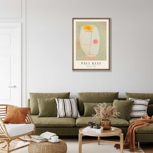 May include: A framed art print featuring a Paul Klee painting titled Untitled, 1934. The artwork displays an abstract, pale oval shape with a soft yellow top, a thin red line, and a small red circle against a muted green background.