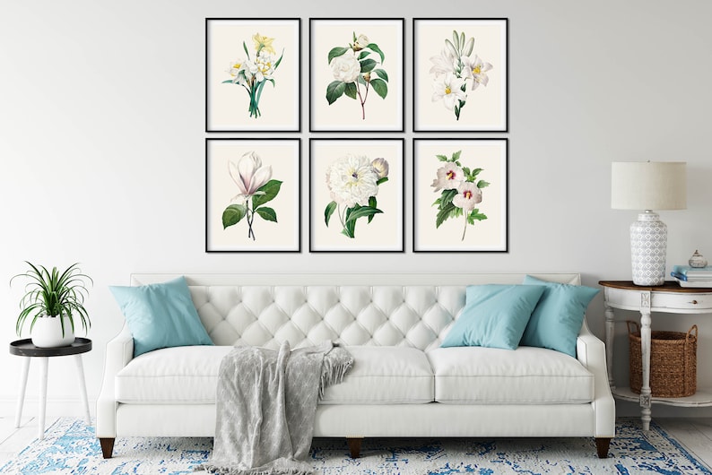 May include: A set of six framed botanical prints featuring white flowers with green leaves. The prints are arranged in a grid pattern on a white wall above a white sofa.