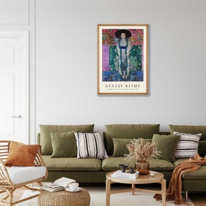 Pu&ograve; includere: Un poster incorniciato di un dipinto di Gustav Klimt intitolato "Ritratto di Adele Bloch-Bauer I" (1907). Il dipinto raffigura una donna con un lungo abito fluido e un grande cappello. Lo sfondo &egrave; un design astratto colorato.