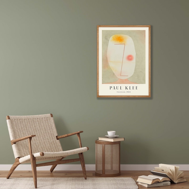 May include: A framed art print featuring a Paul Klee painting titled Untitled, 1931. The artwork displays an abstract, pale oval head shape with a yellow patch, a red dot, and thin red lines on a muted green background, set in a light wood frame.