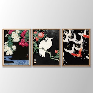 K&ouml;nnte beinhalten: Drei gerahmte Drucke mit japanischer Kunst. Der linke Druck zeigt wei&szlig;e und rosa Blumen auf schwarzem Hintergrund. Der mittlere Druck zeigt einen wei&szlig;en Kakadu, der auf einem Ast mit roten Granatapfelbl&uuml;ten sitzt. Der rechte Druck zeigt rote und wei&szlig;e V&ouml;gel, die vor einem schwarzen Hintergrund fliegen.