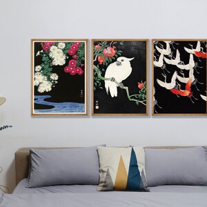 K&ouml;nnte beinhalten: Drei gerahmte Drucke mit schwarzem Hintergrund. Der linke Druck zeigt wei&szlig;e und rosa Blumen mit einem blauen Bach am Boden. Der mittlere Druck zeigt einen wei&szlig;en Kakadu, der auf einem Ast mit roten Blumen sitzt. Der rechte Druck zeigt rote und wei&szlig;e V&ouml;gel, die in einer Schar fliegen.