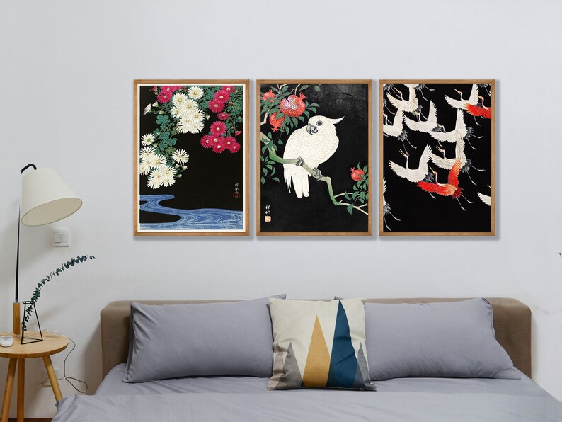 K&ouml;nnte beinhalten: Drei gerahmte Drucke mit schwarzem Hintergrund. Der linke Druck zeigt wei&szlig;e und rosa Blumen mit einem blauen Bach am Boden. Der mittlere Druck zeigt einen wei&szlig;en Kakadu, der auf einem Ast mit roten Blumen sitzt. Der rechte Druck zeigt rote und wei&szlig;e V&ouml;gel, die in einer Schar fliegen.