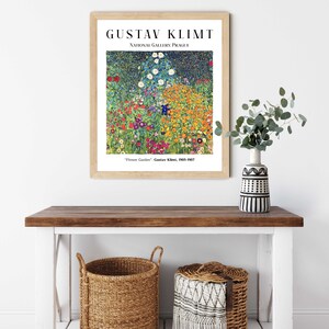 Op de afbeelding: Een ingelijste print van een schilderij van Gustav Klimt getiteld "Bloementuin". Het schilderij toont een levendig veld met bloemen in verschillende kleuren, waaronder rood, geel, oranje, roze en paars. Het schilderij wordt getoond aan een witte muur met een houten lijst.