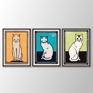 May include: Three framed prints of white cats in different poses. The frames are black and the backgrounds are orange, blue, and green. The prints are dated 1916, 1917, and 1917.