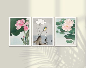 May include: Set of three framed art prints featuring Japanese-style botanical illustrations. The prints depict lotus flowers in various stages of bloom, with pink and white petals, green leaves, and a small bird. The frames are white.