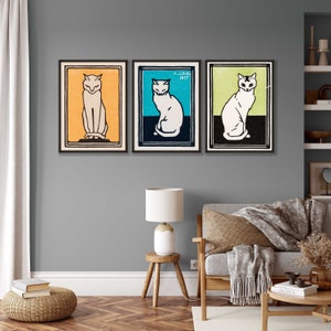 May include: Three framed prints of vintage cat illustrations. Each print features a white cat with black markings, sitting in a different colored background. The backgrounds are orange, blue, and green.